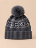 Bonnet cachemire gris foncé à pompon et motif nordique, vue de face sur fond pêche sable