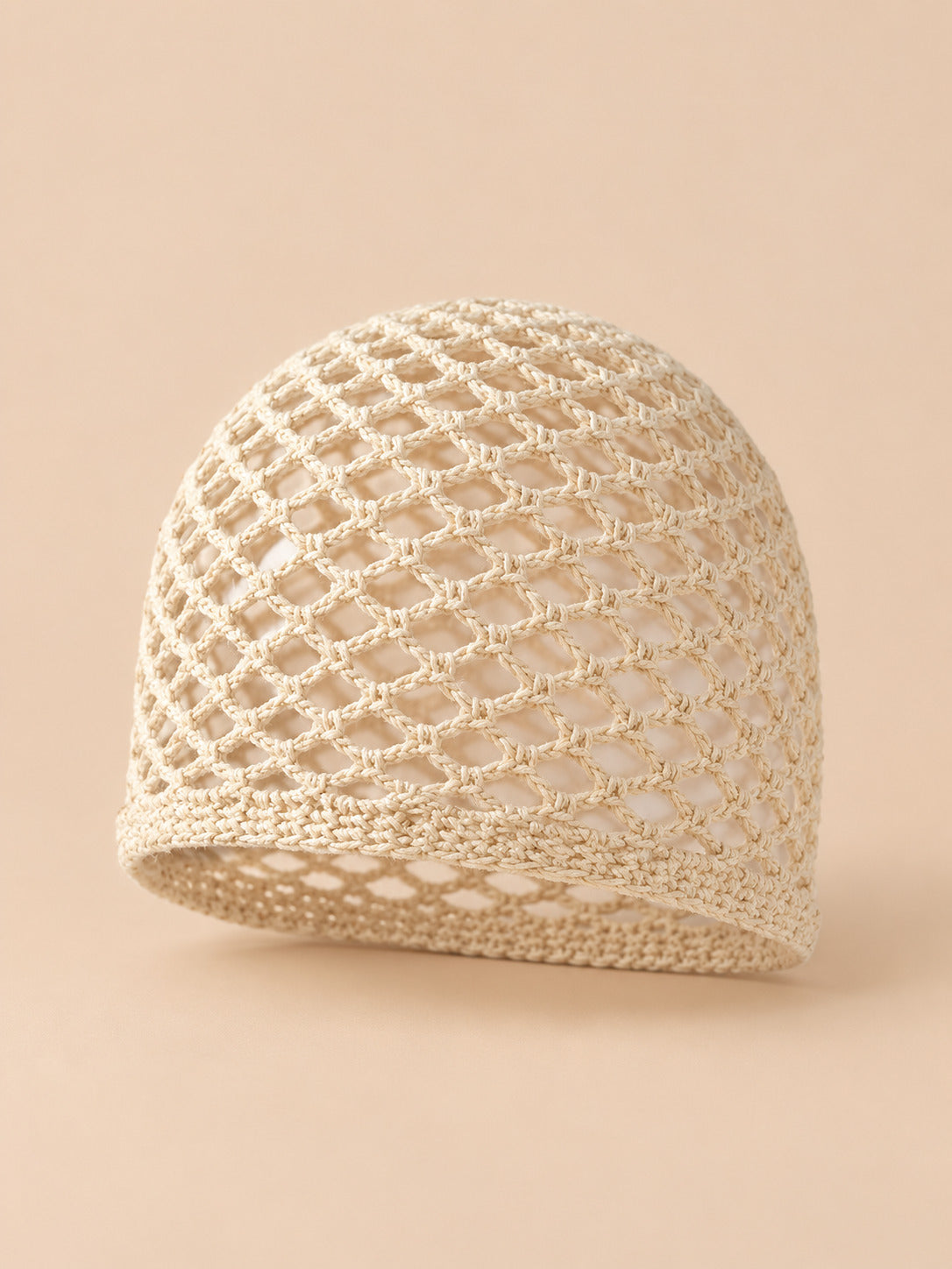 Bonnet fin femme beige en coton résille ajouré, vue trois quarts sur fond pêche sable