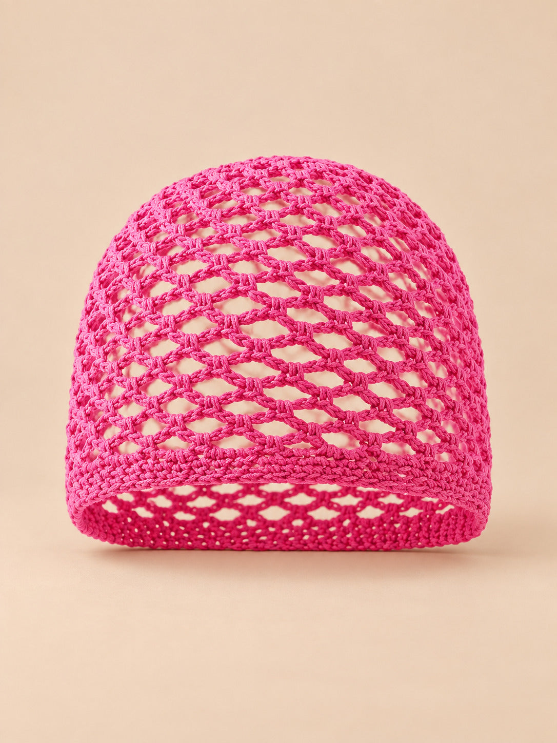 Bonnet fin femme rose fuchsia en coton résille ajouré, vue de face sur fond pêche sable