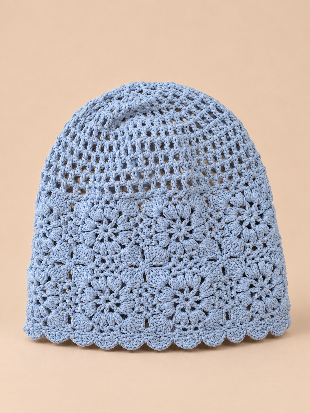 Bonnet turban femme bleu ajouré à fleurs au crochet, vue de face sur fond pêche sable