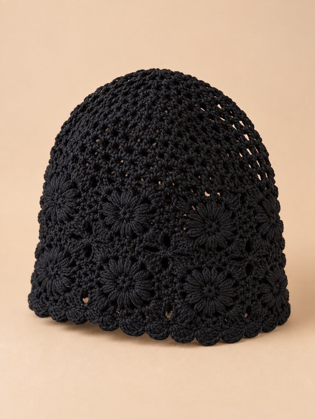 Bonnet turban femme noir ajouré à fleurs au crochet, vue trois quarts sur fond pêche sable
