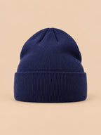 Gorro liso clásico de punto suave y ligero, color azul marino, vista frontal, sobre fondo color arena y melocotón