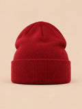 Gorro liso clásico de punto suave y ligero, color burdeos, vista frontal, sobre fondo color arena y melocotón