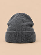 Gorro liso clásico de punto suave y ligero, color gris oscuro, vista frontal, sobre fondo color arena y melocotón